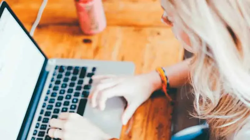 Mujer rubia escribiendo en un portátil sobre una mesa de madera