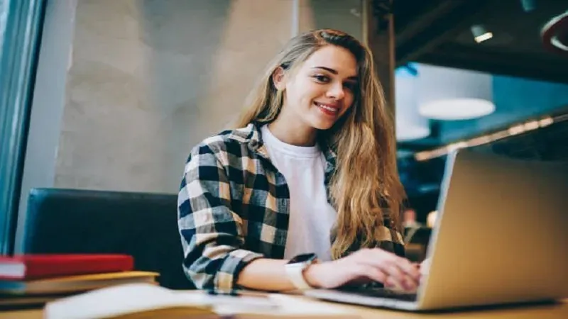 Joven sonriente que trabaja con un portátil en una cafetería
