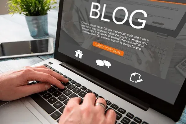 Manos escribiendo en un portátil que muestra la pantalla de un blog