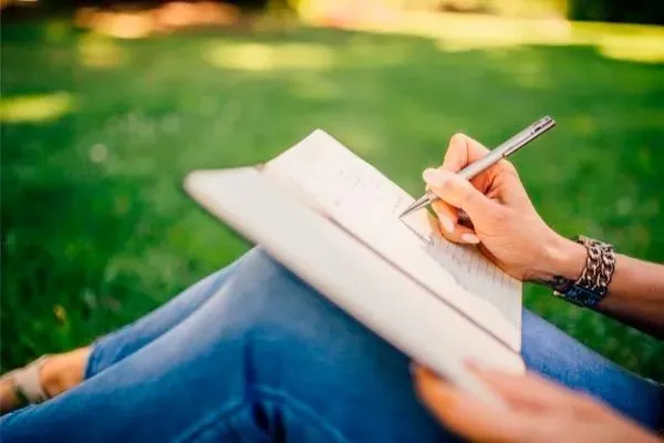 Persona sentada en la hierba escribiendo a mano en un cuaderno