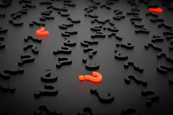 Signos de interrogación negros y dos rojos sobre una superficie oscura