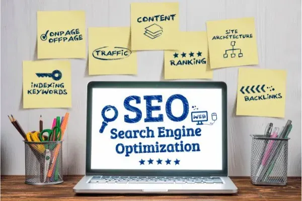 Portátil con las siglas SEO en pantalla rodeado de notas adhesivas con las palabras clave, tráfico y contenido