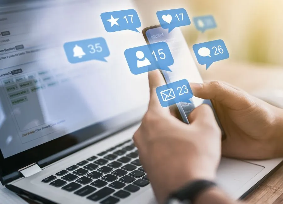 Manos que usan un teléfono móvil con iconos de notificaciones sobre un portátil