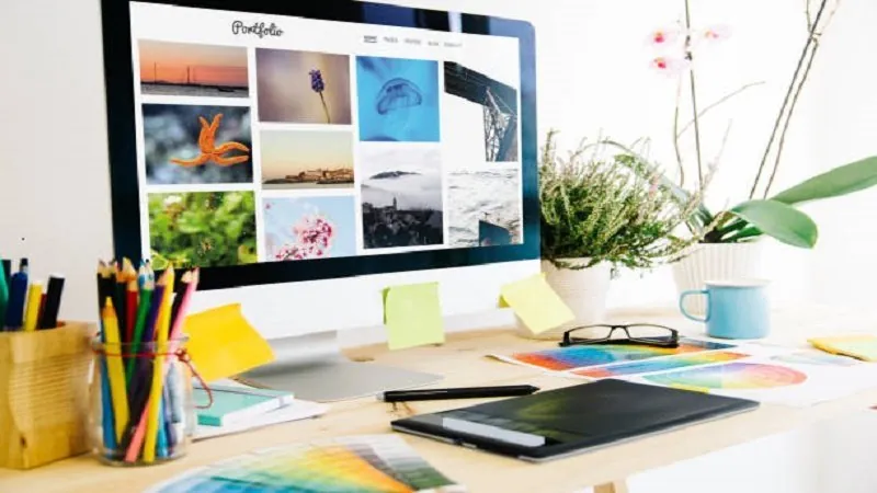 Escritorio con un monitor que muestra un portafolio web, lápices de colores y muestras de color