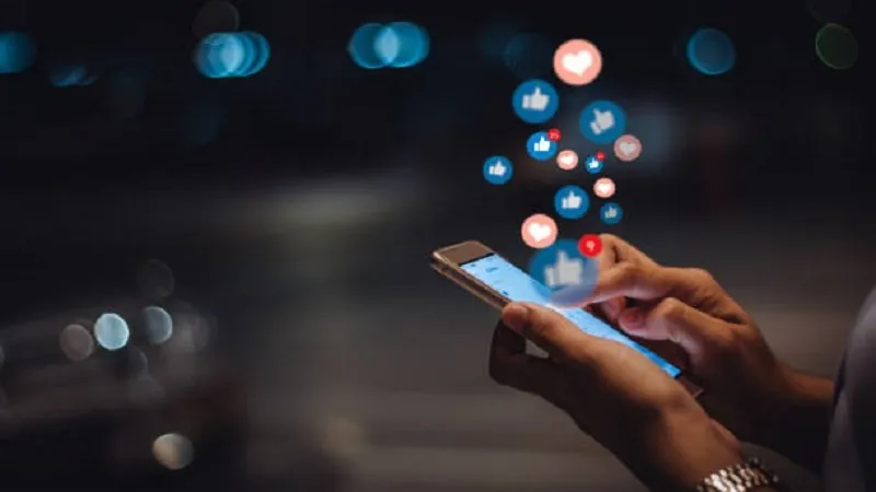 Manos que usan un teléfono móvil con iconos de me gusta flotando sobre la pantalla