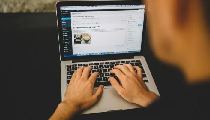Manos escribiendo en un portátil con un editor de blog en pantalla